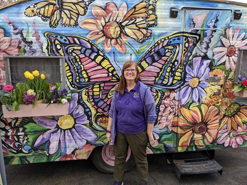 Woman standing in front of colorful pollinator art of butterflies and flowers