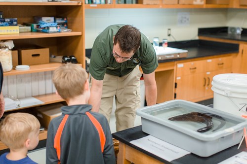 Children examine specimens in a lab with help from an expert