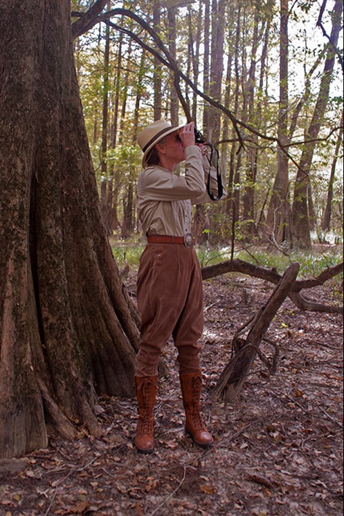 Person in old-fashioned explorer outfit peers through a pair of binoculars